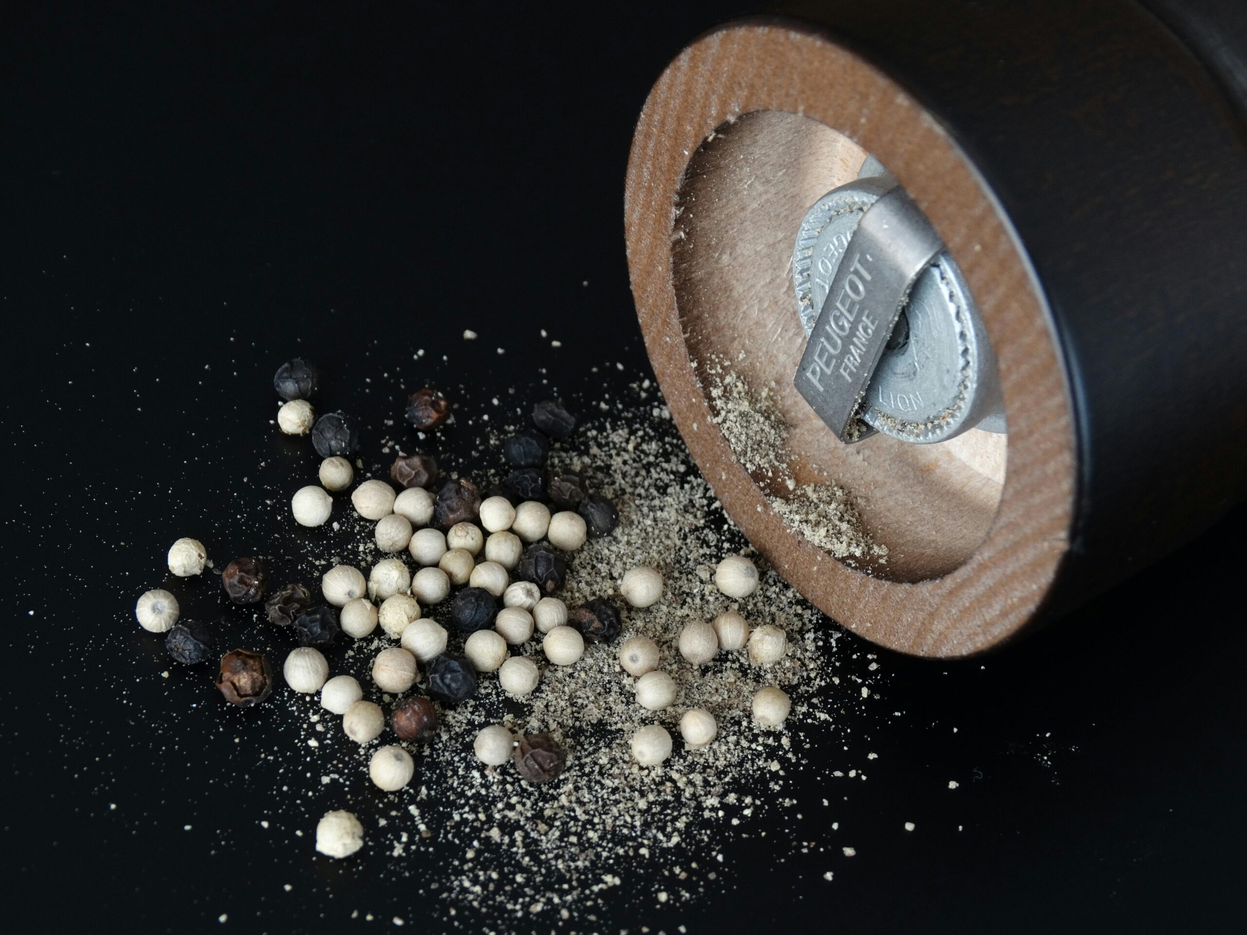 A pepper mill lies on its side, with a mix of whole black and white peppercorns scattered nearby, emphasizing culinary simplicity and flavor